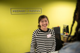 A smiling customer support volunteer happily assists a person at the front desk